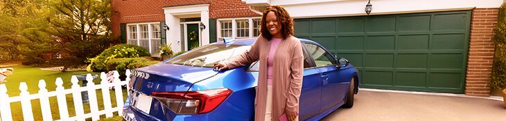 Woman smiling leaning up against a blue car in her driveway with home in background