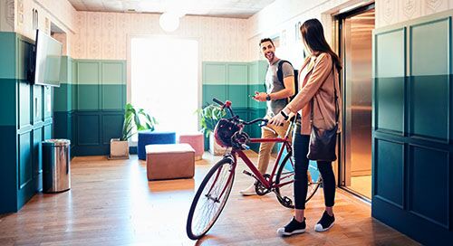 A young man talking to a young woman with her bike in a condo lobby