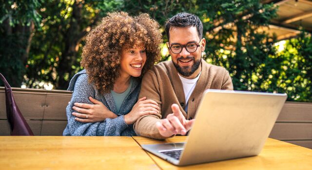 A couple using a laptop outside.