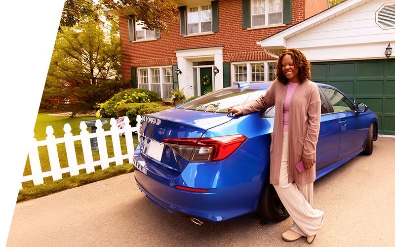 Woman smiling leaning up against a blue car in her driveway with home in background