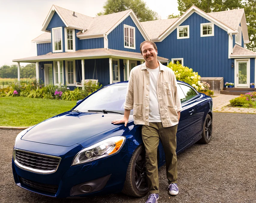 A man standing in front of a blue car and a blue house