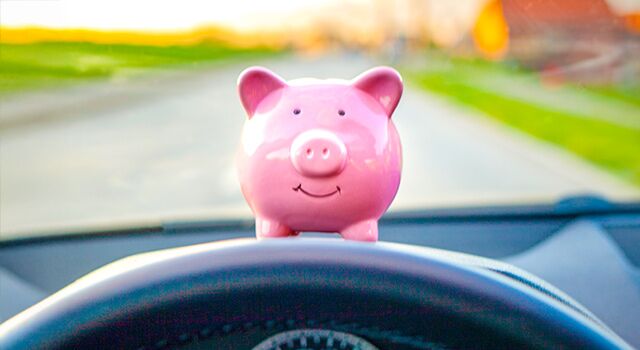 Piggy bank on dashboard of a car with stearing wheel partially in view